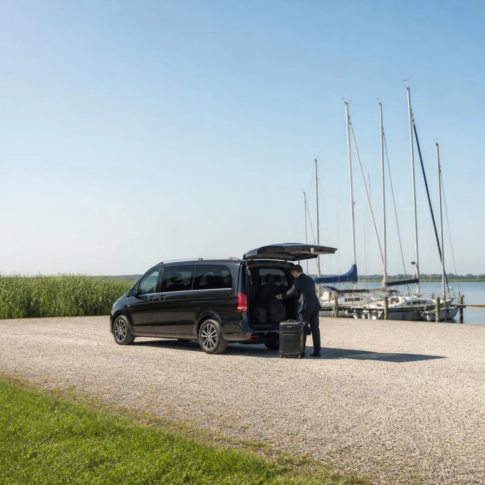 Chauffeur laadt bagage in een zwarte Mercedes V-Klasse bij een jachthaven aan het meer